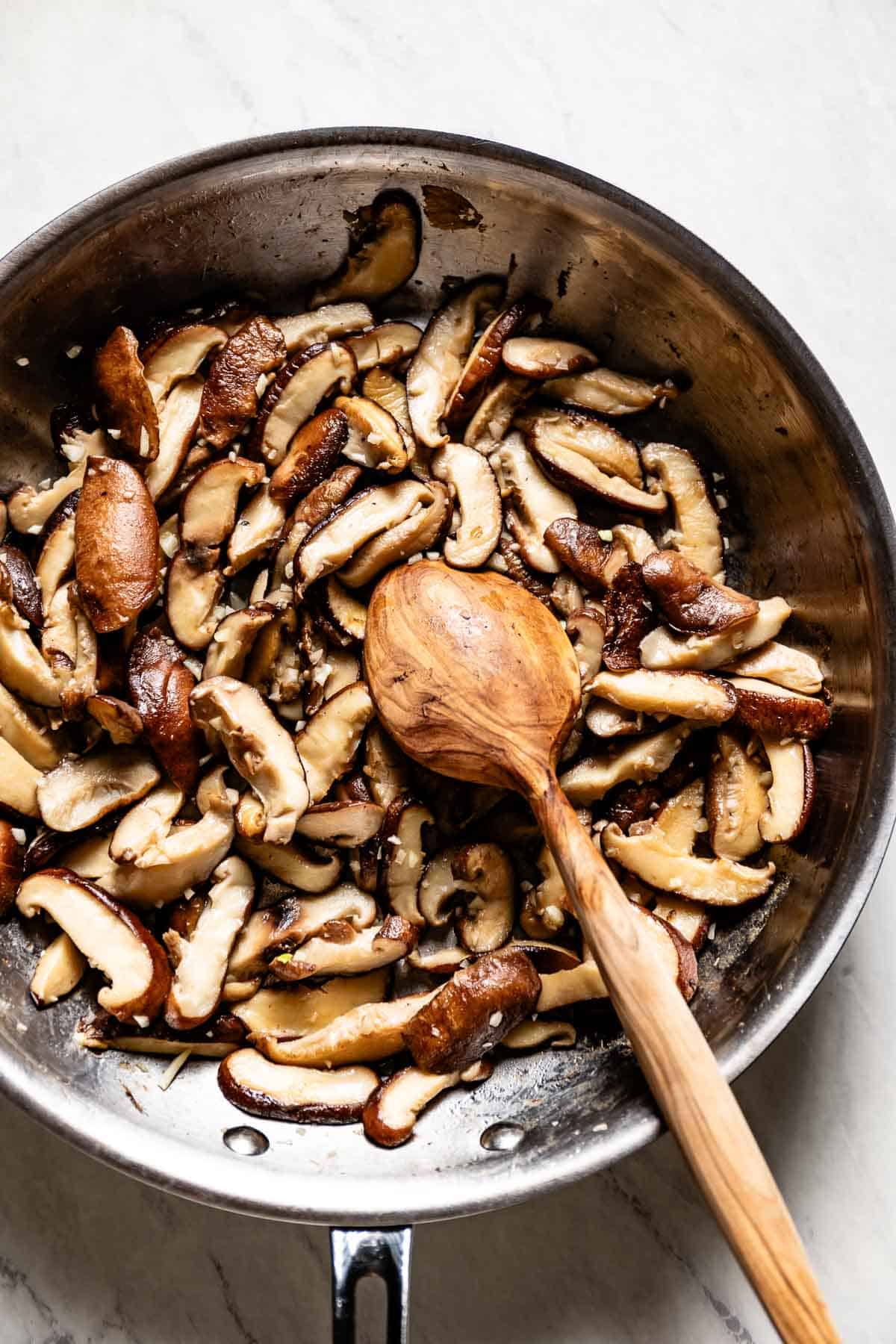 Shiitake mushrooms in a skillet with a spoon on the side.